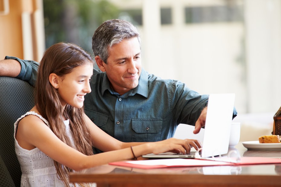 Teenager and her dad use a computer together.