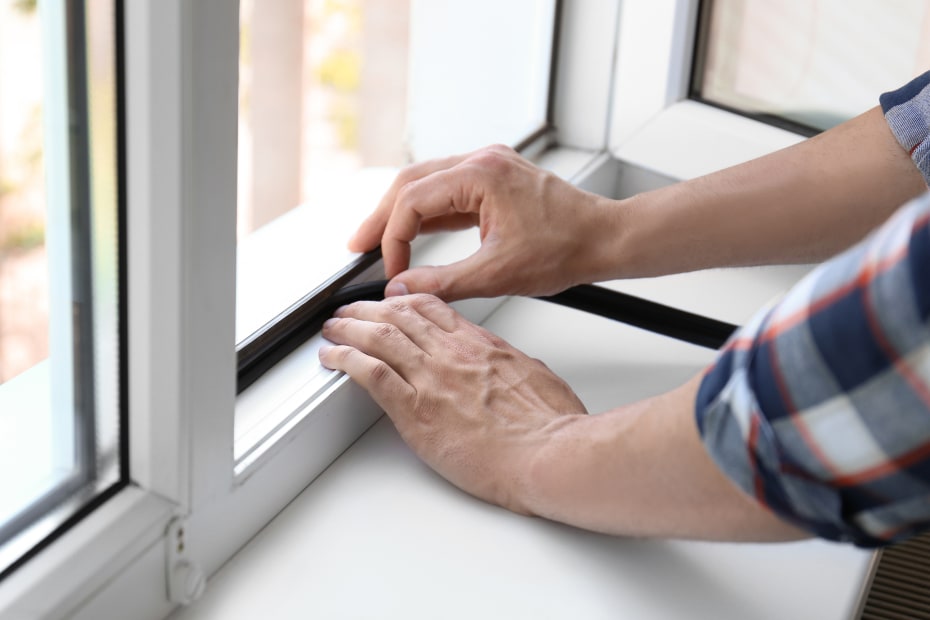 A woman installs weather stripping around a window.