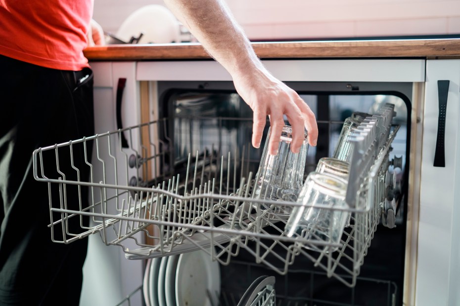 A man puts a glass in a dishwasher.