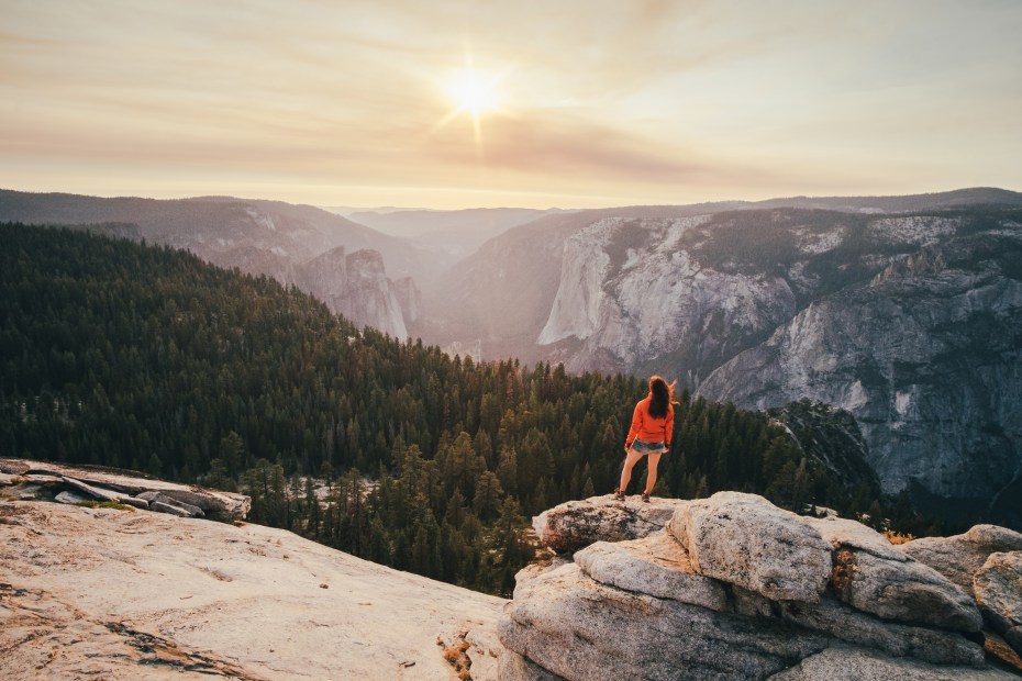 A hiker stands on a rock overlooking Yosemite Valley at sunset.
