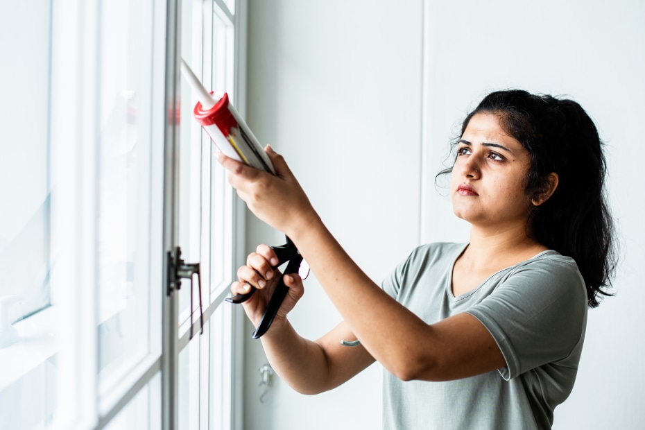 A woman caulks around a window.