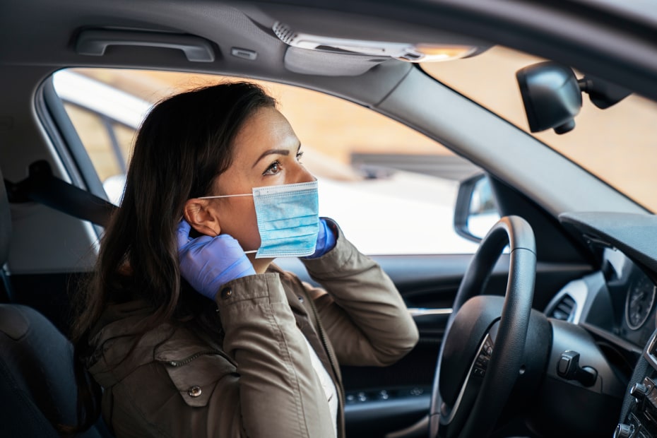 A woman puts on a mask in her car.