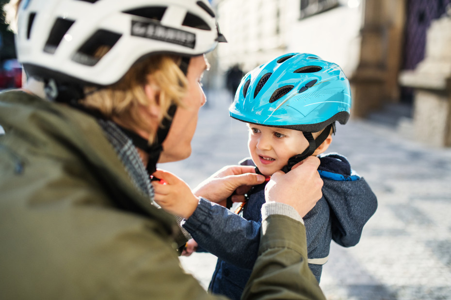 A dad buckles a blue helmet onto his toddler.