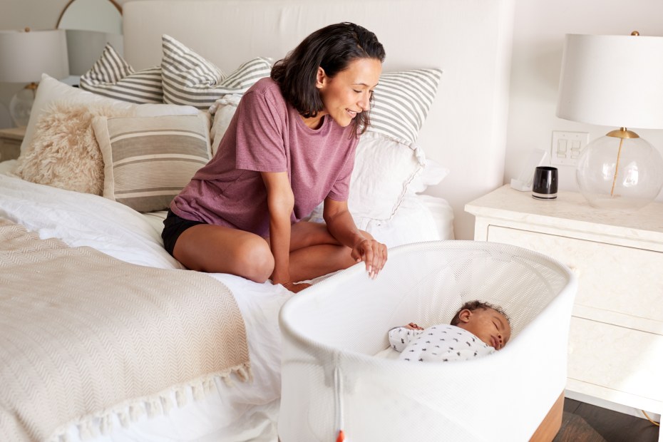 A woman looks at her baby in a bassinet.