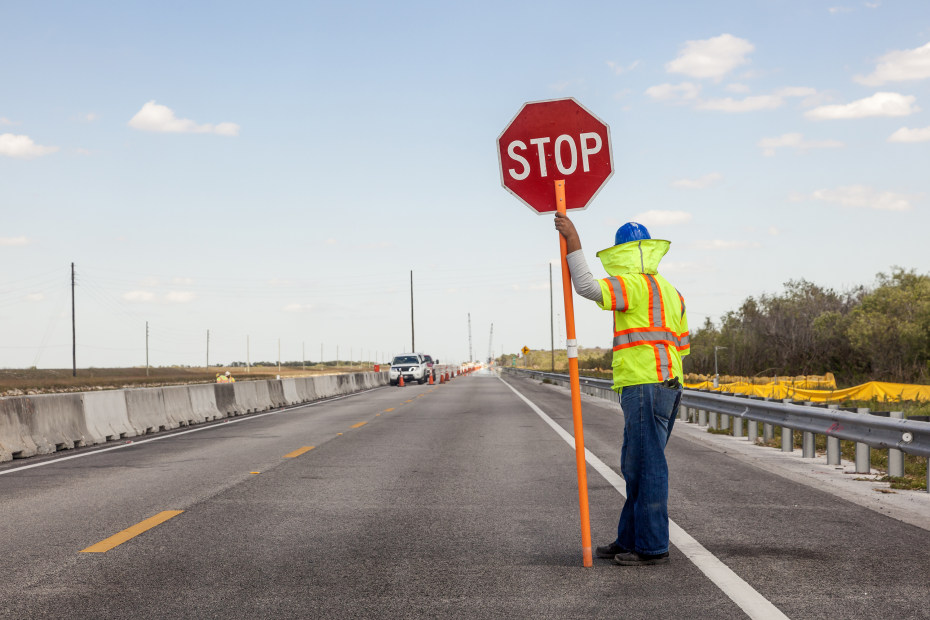 A road worker holds up a stop sign on a highway.