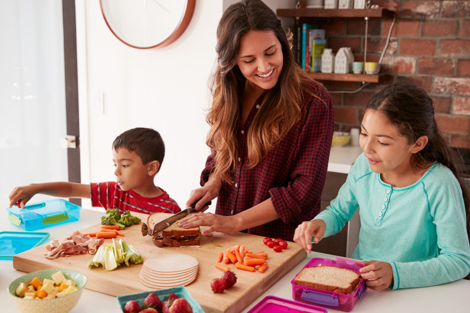 A mom and her two children prepare sandwiches and snacks.