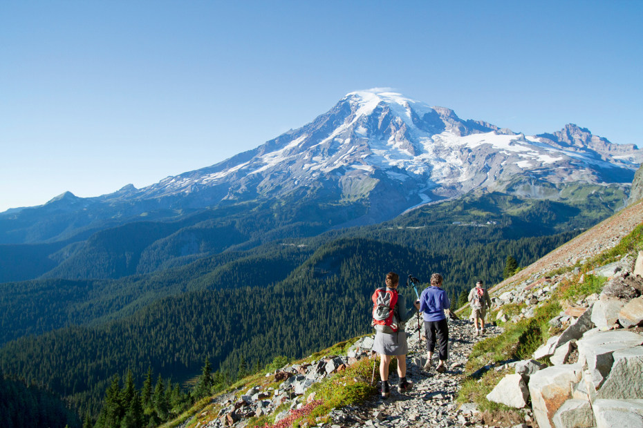 three backpackers on a trail hike towards Pinnacle Peak, in background, at Mount Rainier National Park