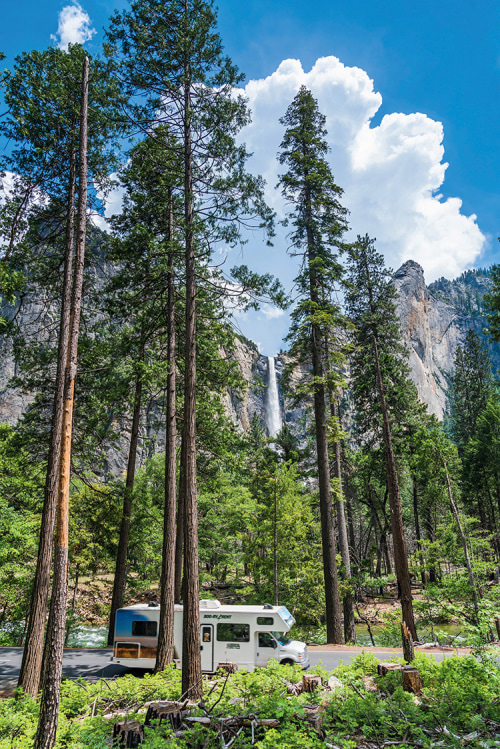 RV drives past redwood trees and a waterfall.