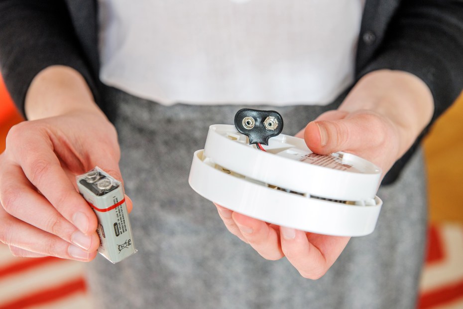 A woman replaces the battery in a smoke detector.