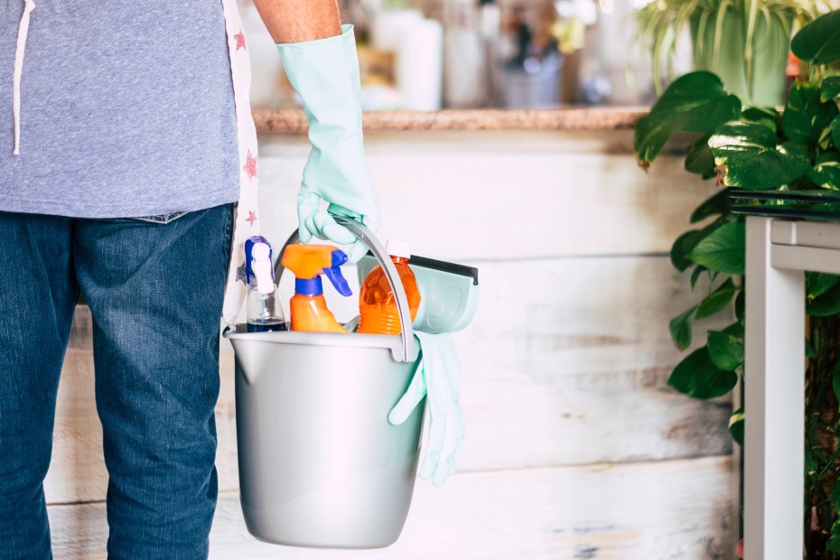 a man holds a bucket of cleaning supplies with a gloved hand