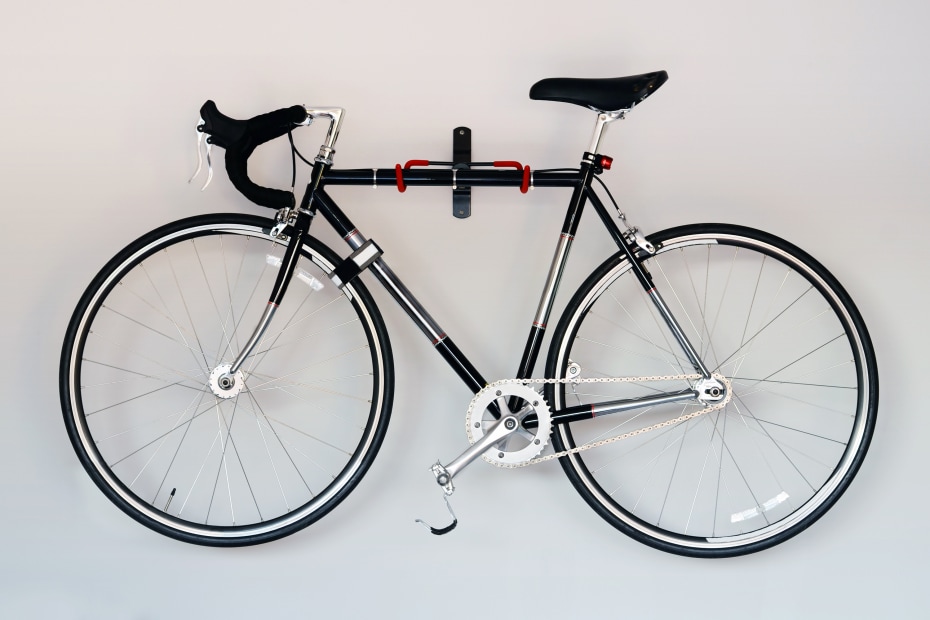 A black road bike hangs on a white wall.