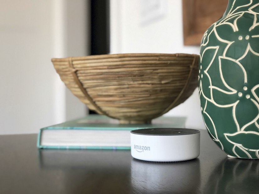 an Amazon Echo Dot smart home device sits on table by two ceramic bowls and book