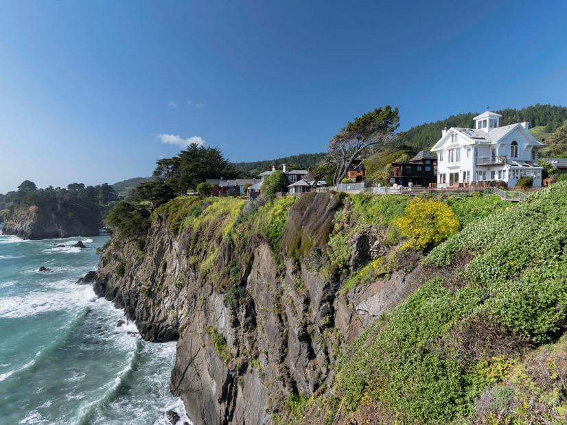 array of historic buildings perched cliffside overlooking the sea on a near cloudless, sunny  day on the Mendocino coast