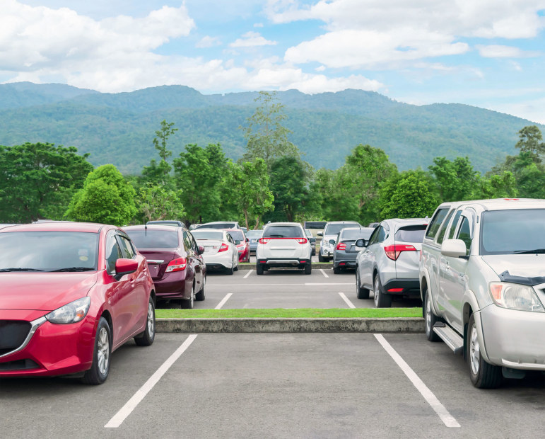 Parking lot, nearly full with red, maroon, white, and silver sedans