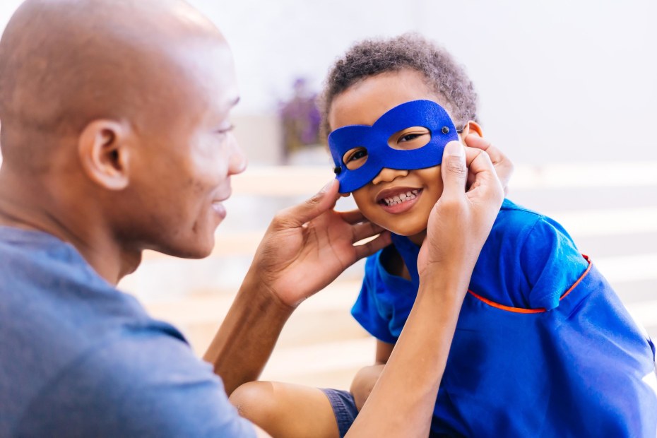 a dad adjusts a blue superhero mask on his son