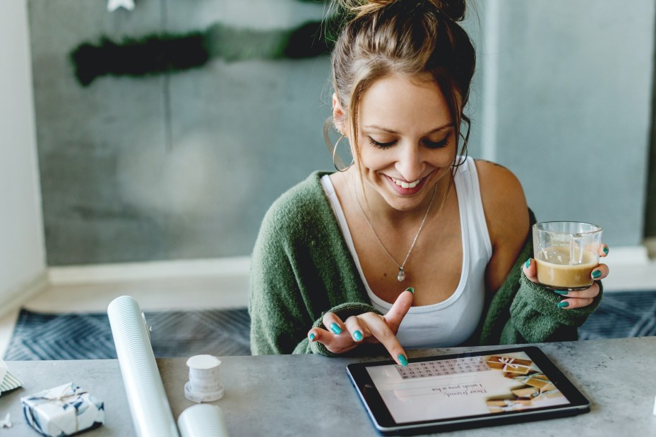 a smiling young woman looks on a mobile device to order presents 