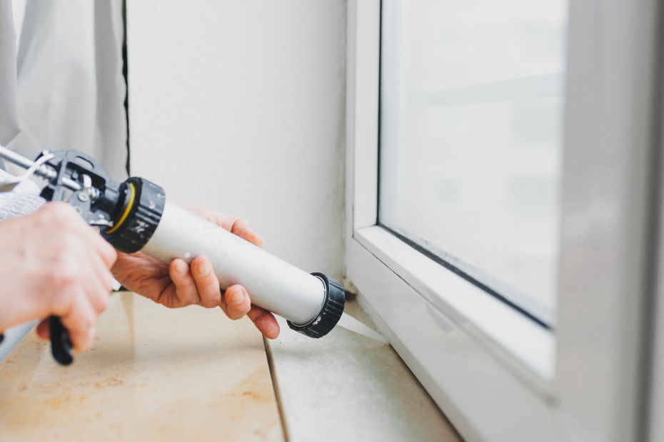 A woman caulks the edge of the window sill.