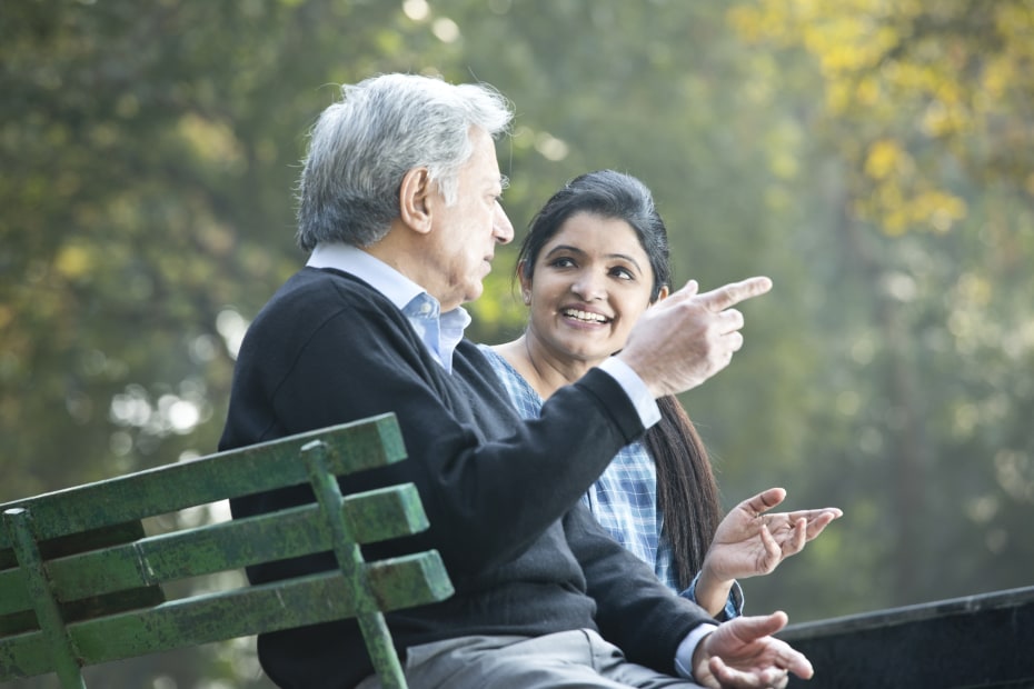 an elderly father speaks with his adult daughter on a park bench