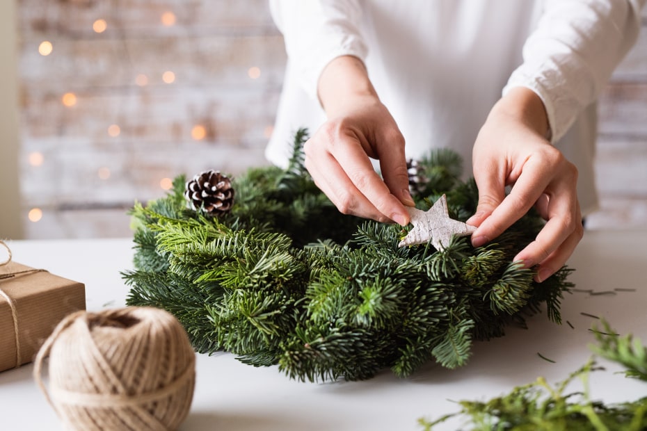 A woman makes a wreath with evergreen branches.