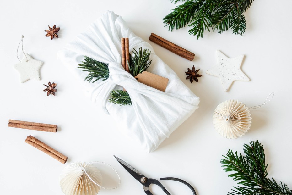 A package in reusable wrapping with fir branches and cinnamon sticks.
