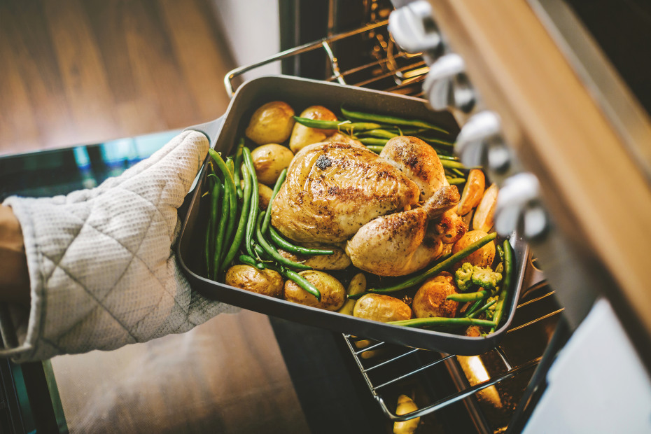 A home cook removes a roast chicken with green beans and potatoes from the oven.