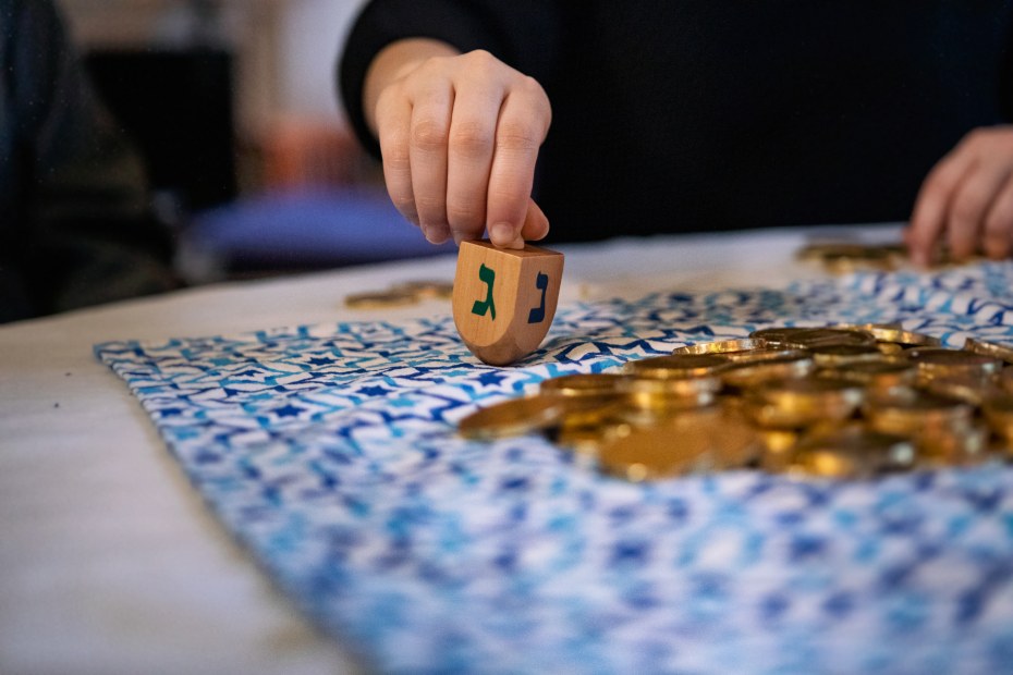 a hand spins a wooden dreidel with golden coins piled on a table