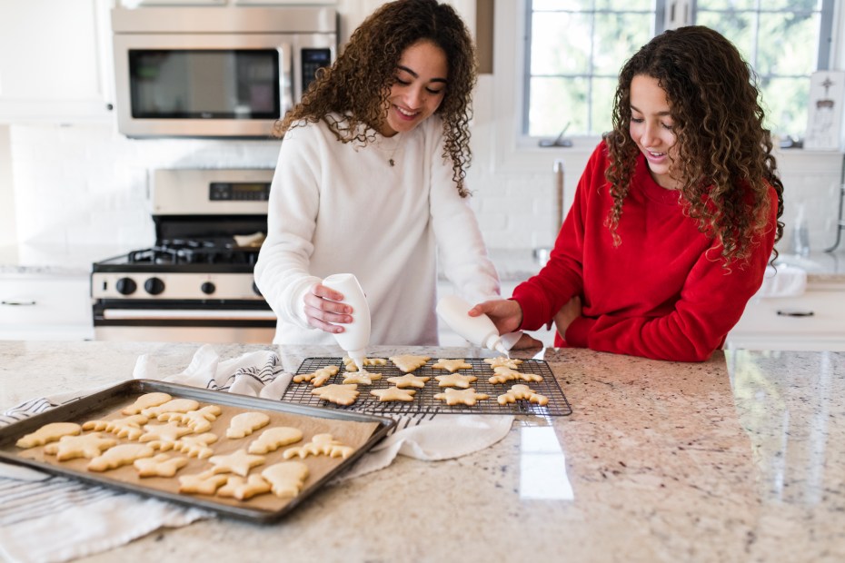 two sisters ice holiday cookies in a modern kitchen