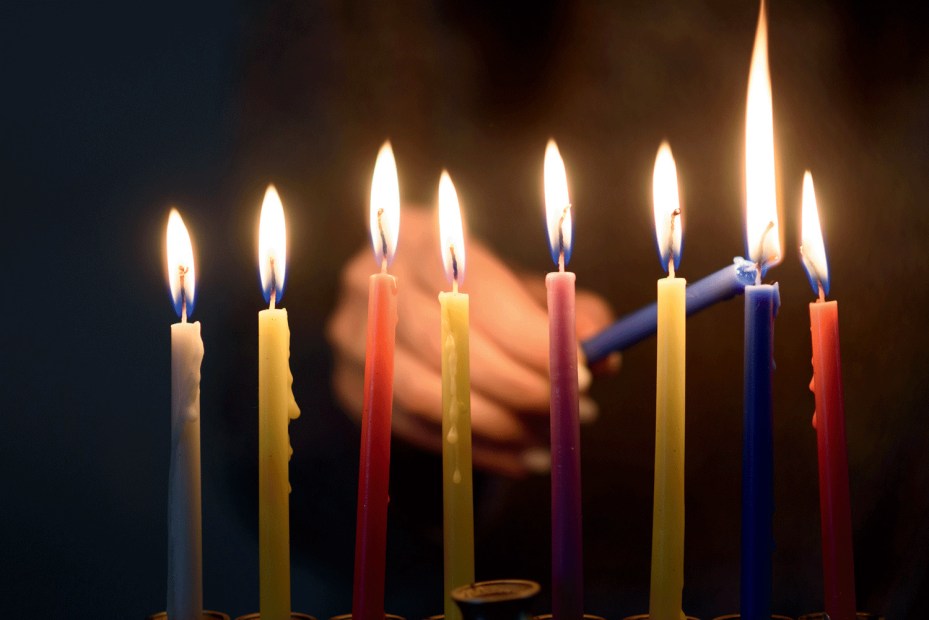 tapered Hanukkah candles in assorted colors being lit in dark room