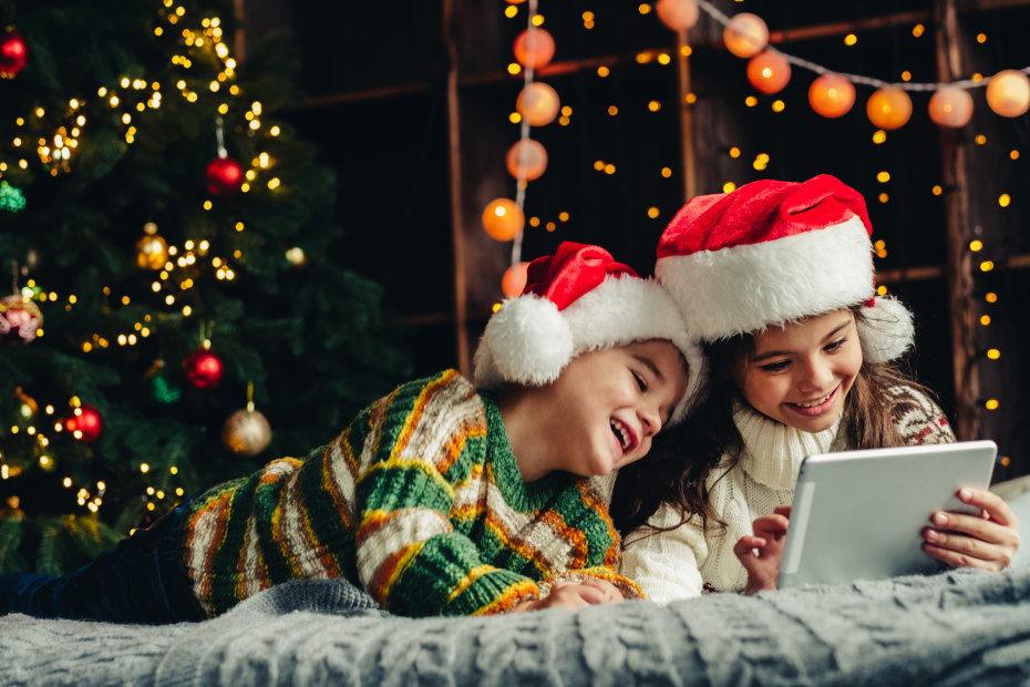 Siblings watch a holiday movie together with Santa hats on.