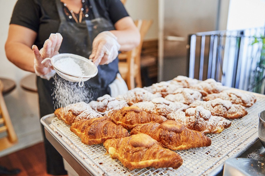 bakery worker sifts powdered sugar over a tray of freshly-baked almond croissants at Arsicault Bakery in San Francisco's Inner Richmond neighborhood