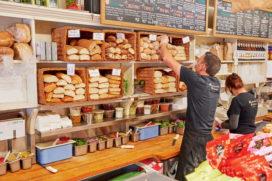 sandwich maker, masked for Covid, reaches for bread at Lucca Delicatessen in San Francisco's Marina District