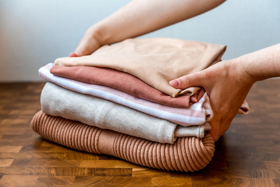 A woman picks up a stack of peach colored clothing.