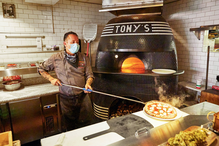 Pizza baker, wearing Covid mask, removes a fresh pie from the oven at Tony's Pizza Napoletana in San Francisco's North Beach neighborhood