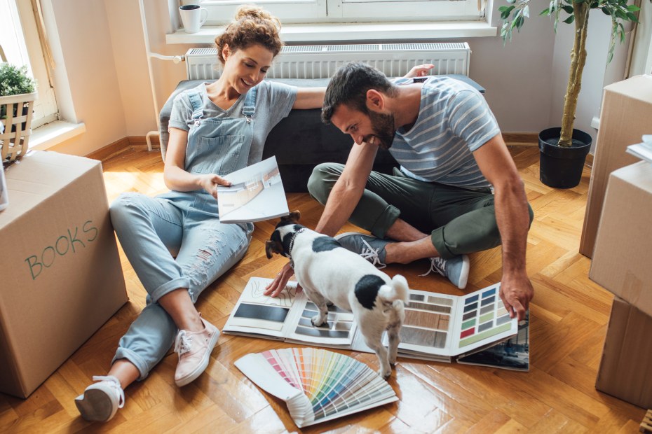 A couple sit on the floor and flip through paint samples.