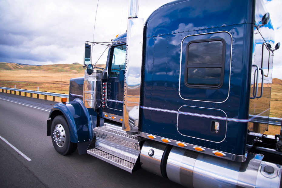 A blue semi truck drives on the highway in California.