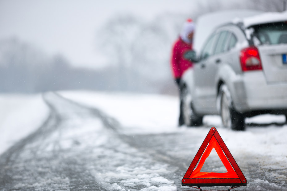 Reflective triangle on a snow-covered road in front of a broken down car.