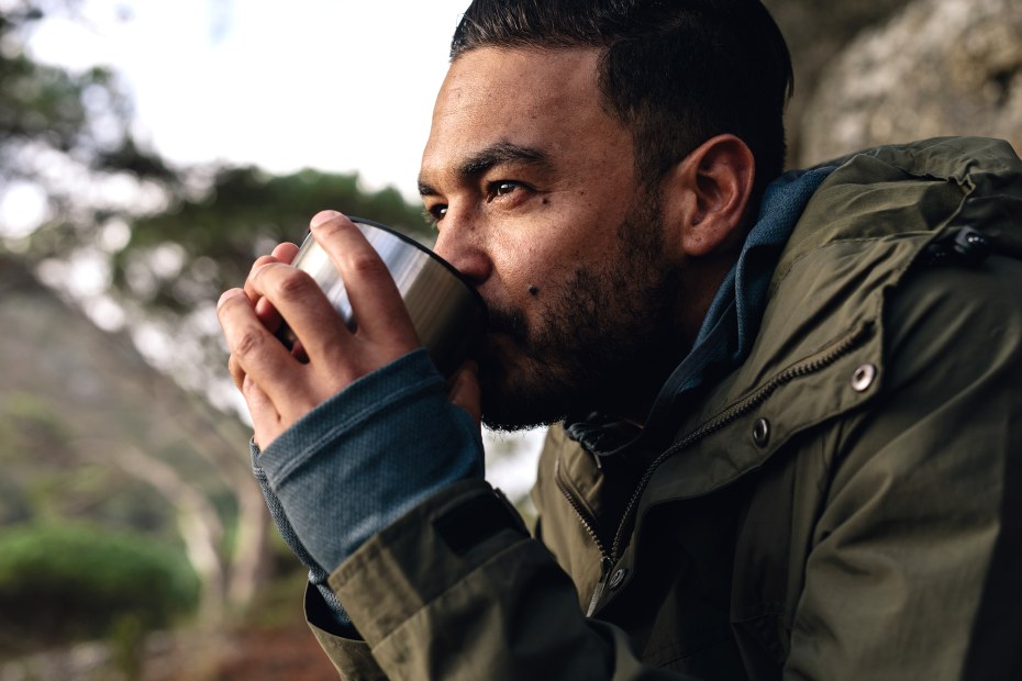 A hiker takes a sip from an insulated mug.