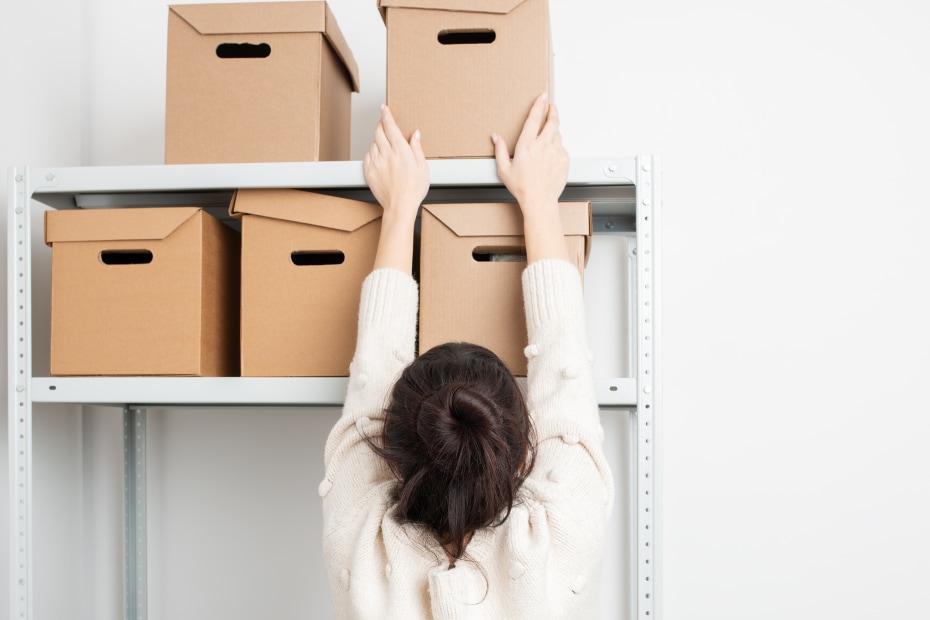 A woman removes a box from a shelf in her garage.