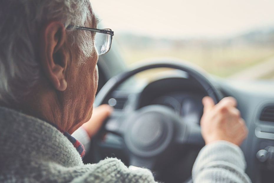 A senior man driving during the day with glasses on.