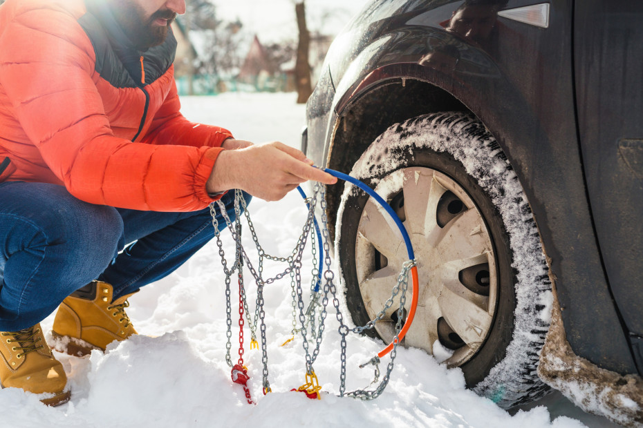 A driver installs chains on the front tire of their car.