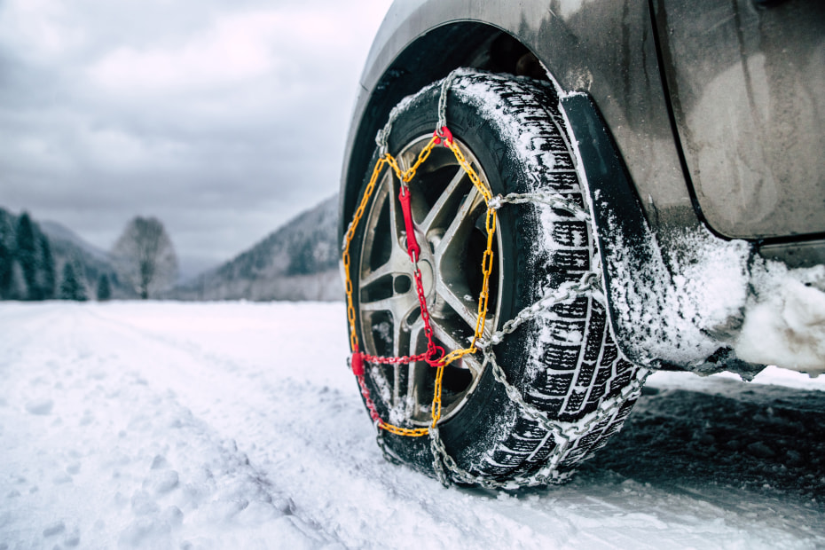 Chains wrapped around a front tire on a snow-covered road.