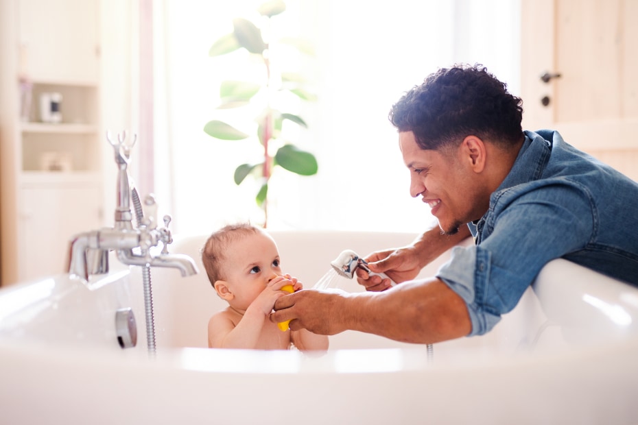 A dad washes his baby in a freestanding bathtub.