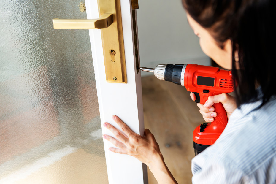 A woman fixes a doorknob with a power drill.