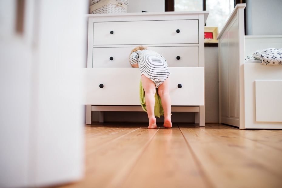 A toddler leans over an open dresser drawer.