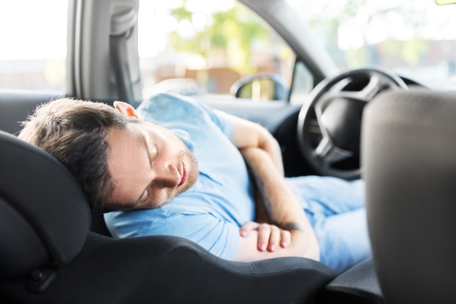 A driver sleeps in his car at a rest stop.