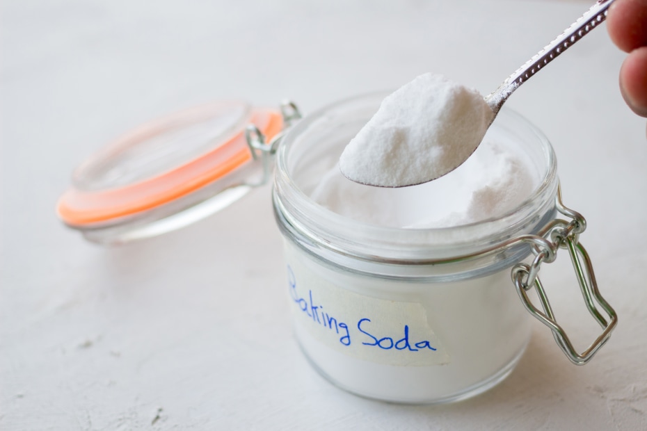 A person takes a heaping spoonfull of baking soda out of a jar.