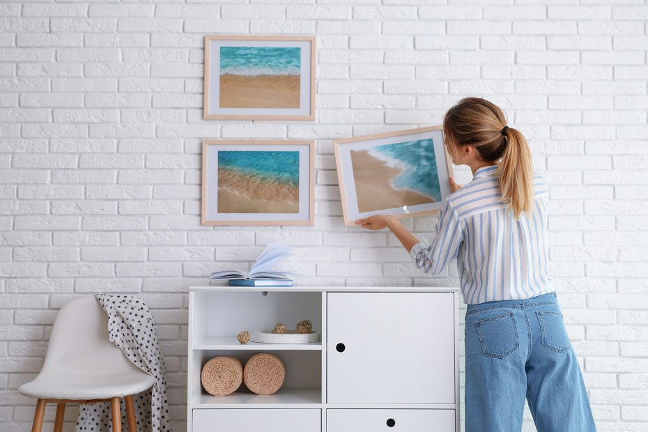 A woman hangs a photo on a brick wall.