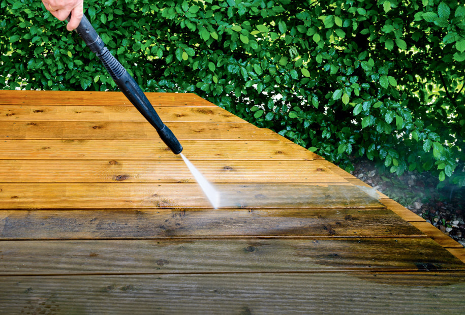 A homeowner pressure washes their deck.