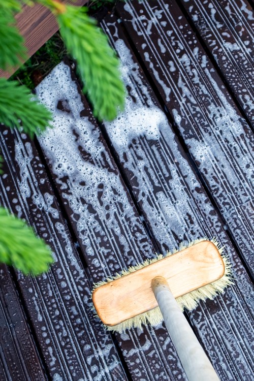 A homeowner cleans their deck with a bristled brush and biodegradable soap.