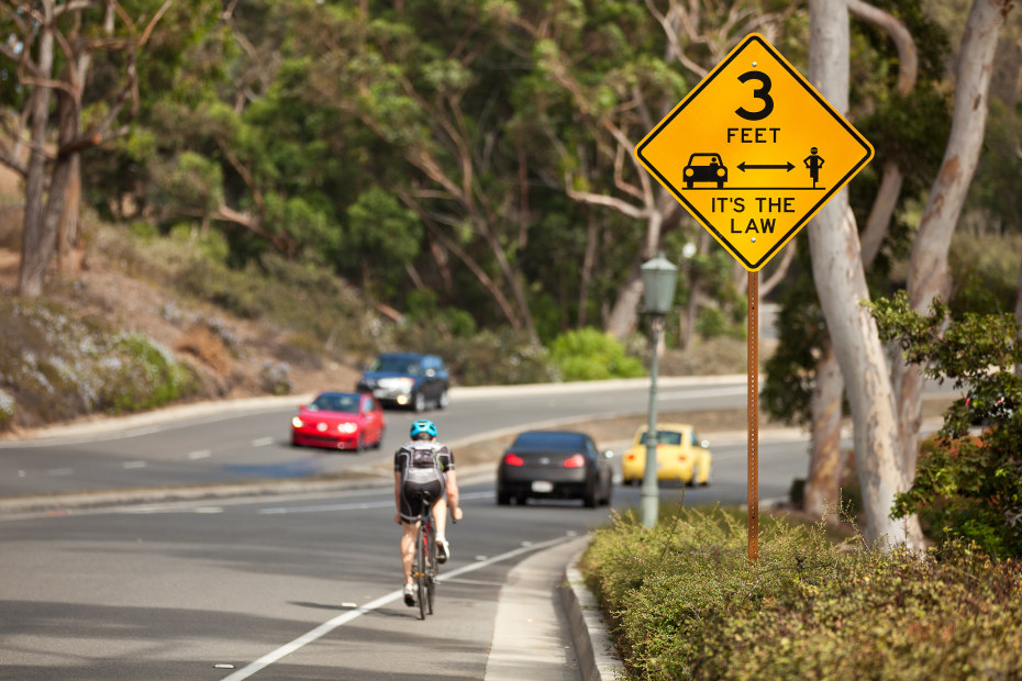A cyclist rides past a pass with at least 3 feet sign.